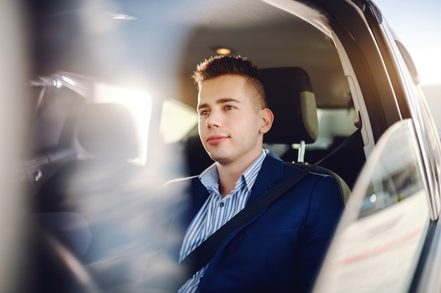 Młody wyrafinowany kaukaski mężczyzna ubrany elegancko, swobodnie prowadzący samochód i patrząc na autostradę.