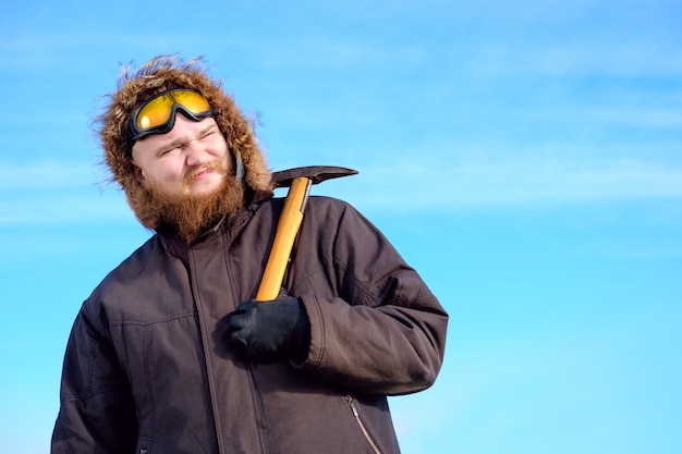 Młody wysoki brodaty odkrywca polarny w okularach ochronnych na czole z lodową siekierą