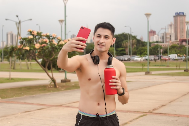 Młody wysportowany mężczyzna bez koszulki robi selfie na placu.