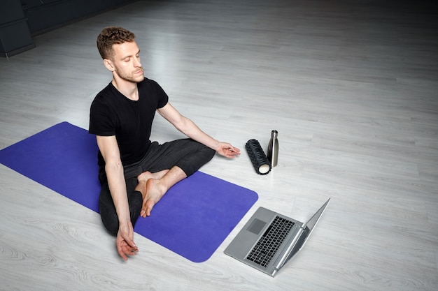 Młody, wysportowany mężczyzna medytuje przed laptopem