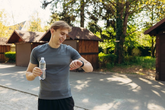 Młody wysportowany mężczyzna pije wodę po treningu Facet fitness trzyma plastikową butelkę odpoczywa po treningu w parku koncepcja zdrowego stylu życia