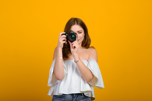 Młody żeński fotograf z kamerą nad żółtym tłem