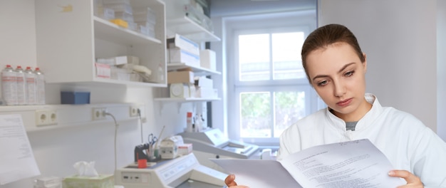 Młody żeński naukowiec czyta drukowane notatki w laboratorium naukowym, panoramiczny wizerunek