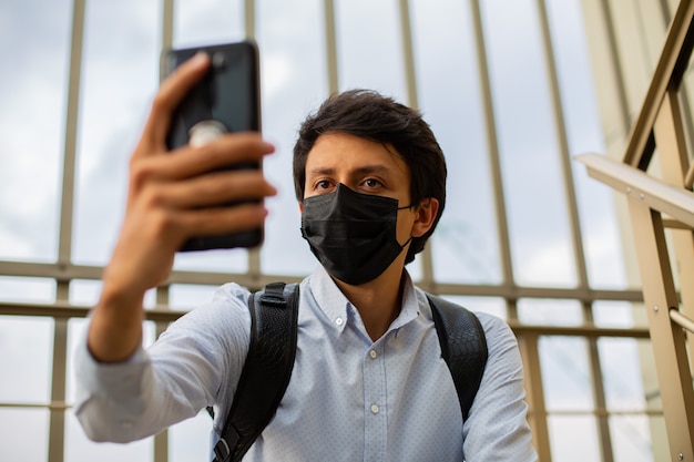 Młodych Mężczyzn Z Maską Siedzi Na Schodach Z Posiłkiem I Trzyma Telefon W Rękach, Biorąc Selfie