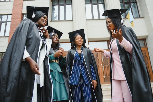 Młodzi absolwenci stojący przed budynkiem uniwersytetu w dniu ukończenia szkoły gra