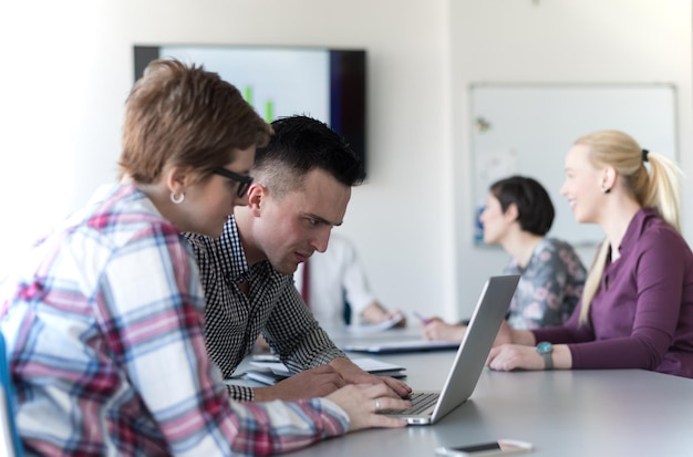 młodzi biznesowi startupowcy, para pracująca na laptopie, grupa przedsiębiorców na spotkaniu w tle we wnętrzu biura