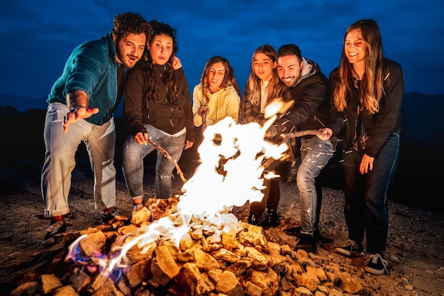 Młodzi ludzie bawią się razem na nocnej imprezie przy ognisku Koncepcja stylu życia Wanderlust ze szczęśliwymi przyjaciółmi podróżnikami rozgrzewającymi się przy ognisku o zmierzchu Żywy filtr kontrastowy