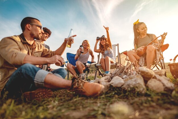 Młodzi ludzie dobrze się bawią na łonie natury. Odpoczywają, śmieją się i śpiewają przy muzyce z ukulele, szczęśliwi, że są razem.