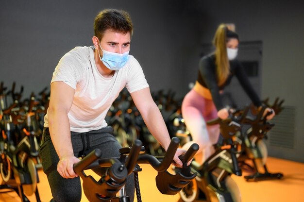 Zdjęcie młodzi ludzie kręcenie się na siłowni fitness z maską ochronną podczas epidemii koronawirusa.