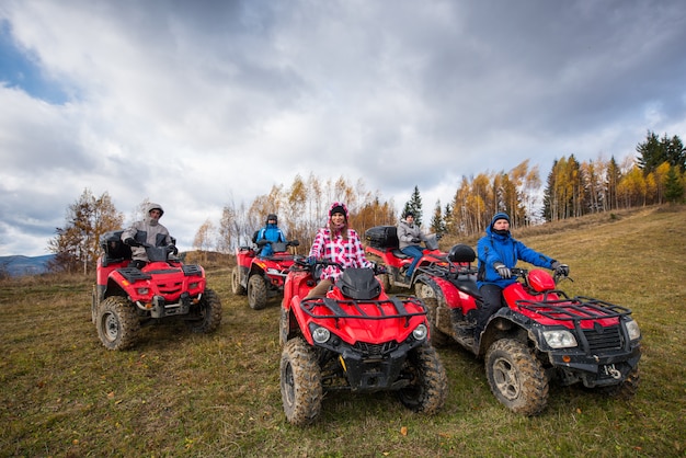 Młodzi ludzie na czerwonych atv terenowych pojazdach na wsi wlec w naturze pod niebem z chmurami