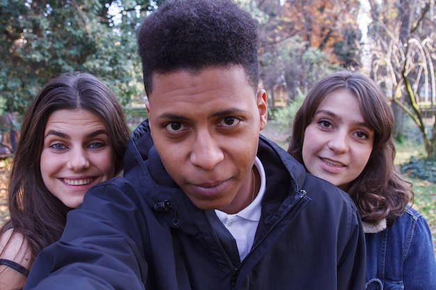 Młodzi ludzie różnych ras robiący sobie selfie smartfonem w parku