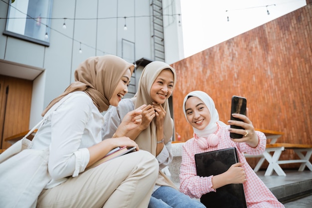 Młodzi ludzie siedzący na schodach robiący selfie z telefonami komórkowymi na tle budynków