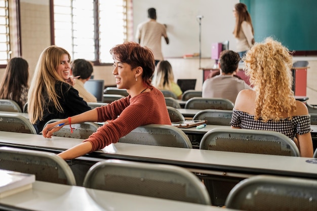 Młodzi ludzie w klasie uniwersyteckiej rozmawiają, podczas gdy kolega z klasy wyjaśnia koncepcję nauki i edukacji na tablicy