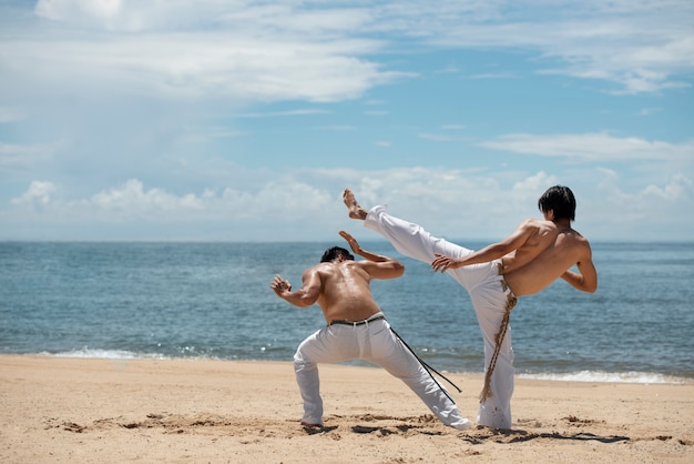 Zdjęcie młodzi mężczyźni bez koszuli ćwiczą razem capoeirę na plaży