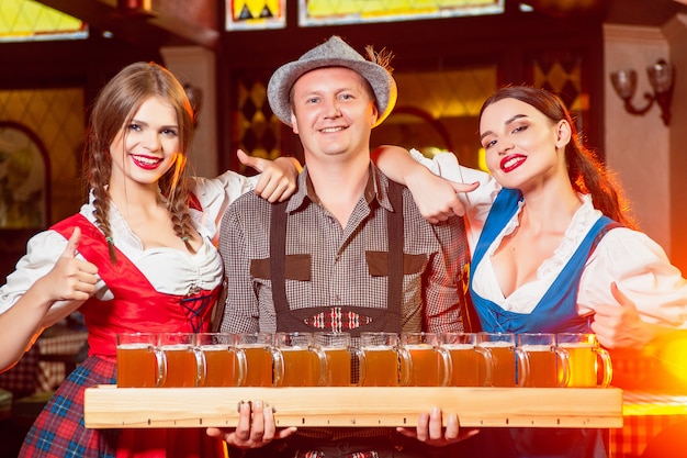 Młodzi Piękni Kelnerzy W Strojach Ludowych Na Imprezie Oktoberfest Z Ogromną Tacą Po Piwie.