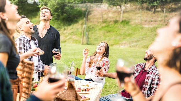 Młodzi przyjaciele bawią się pijąc czerwone wino na pikniku z grilla na przyjęciu w ogrodzie