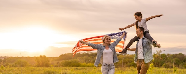 Młodzi rodzice z córką trzymając amerykańską flagę na wsi o zachodzie słońca. Obchody Święta Niepodległości.