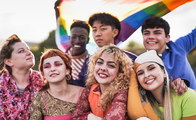 Młodzi, różnorodni ludzie bawią się podczas parady dumy LGBT trzymając tęczową flagę