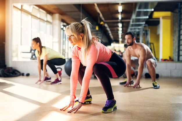 Młodzi zmęczeni sportowcy na siłowni rozciągają mięśnie nóg po zajęciach pilates.