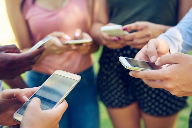 Mobilni milenialsi Przycięte zdjęcie grupy przyjaciół używających razem telefonów na zewnątrz
