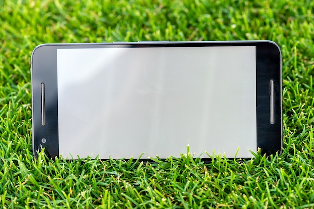 Zdjęcie mobilny mądrze telefonu mockup z bielu ekranem na zielonej trawy tle.
