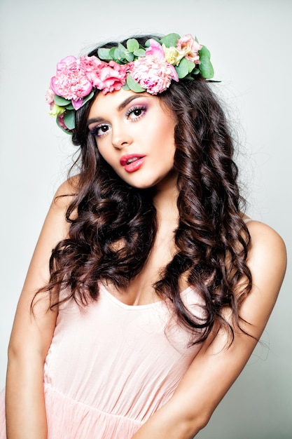 Moda brunetka kobieta z długimi falującymi włosami i wiosennymi kwiatami wieniec na tle