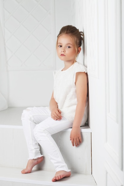 Moda Dziecięca Piękna Zamyślona Poważna Blondynka W Białych Ubraniach Siedzi I Pozuje