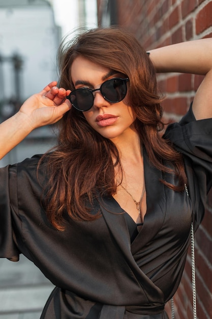 Moda elegancka ładna dama w czarnej stylowej sukience nosi okulary przeciwsłoneczne i pozuje w mieście