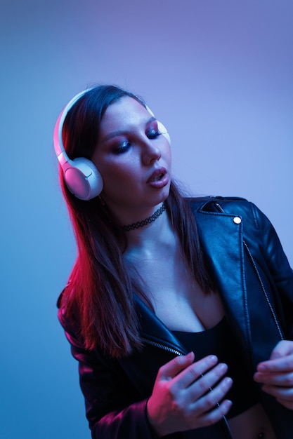 Moda kobieta ze słuchawkami słucha muzyki na neonowym tle w studio