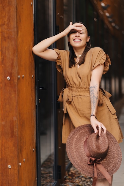 Moda młoda kobieta ubrana w letnią sukienkę z szerokim kapeluszem z wikliny spacery i pozuje na starym mieście.