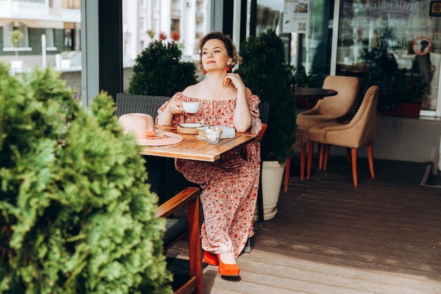 Moda plenerowa portret pięknej kobiety siedzącej w kawiarni piję kawę i czytam starą książkę kobieta w sukience i kapeluszu
