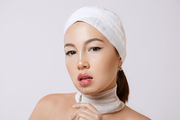 Moda portret młodej pięknej azjatyckiej kobiety na na białym tle ze strzykawką w dłoniach strzykawka zawiera zastrzyki leków dla kosmetologii