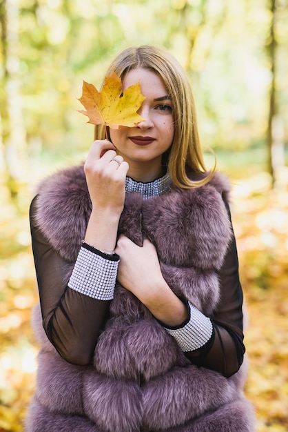 Moda ubiera kobietę w futro i sukienkę pozuje w jesiennym parku