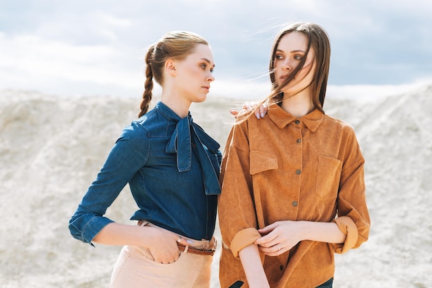 Moda uroda portret młodych kobiet sióstr w brązowych organicznych aksamitnych koszulach dżinsowych na tle pustyni