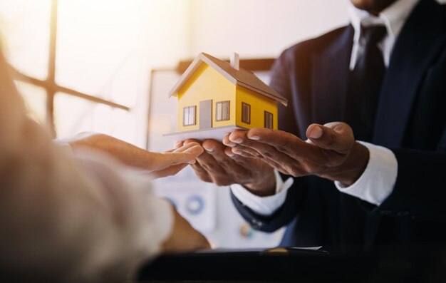 Model domu z agentem nieruchomości i klientem omawiającym umowę na zakup ubezpieczenia domu lub pożyczkę koncept nieruchomości