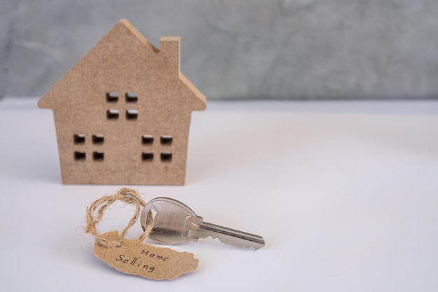 Model małego brązowego drewnianego domu i etykieta sprzedaży domu przymocowana do klucza do domu. Koncepcja nieruchomości, hipoteka, wynajem, kup dom