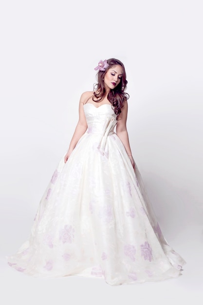 Model ubrany w suknię ślubną, z fryzurą i kwiatem w jej fryzurę, na białym tle
