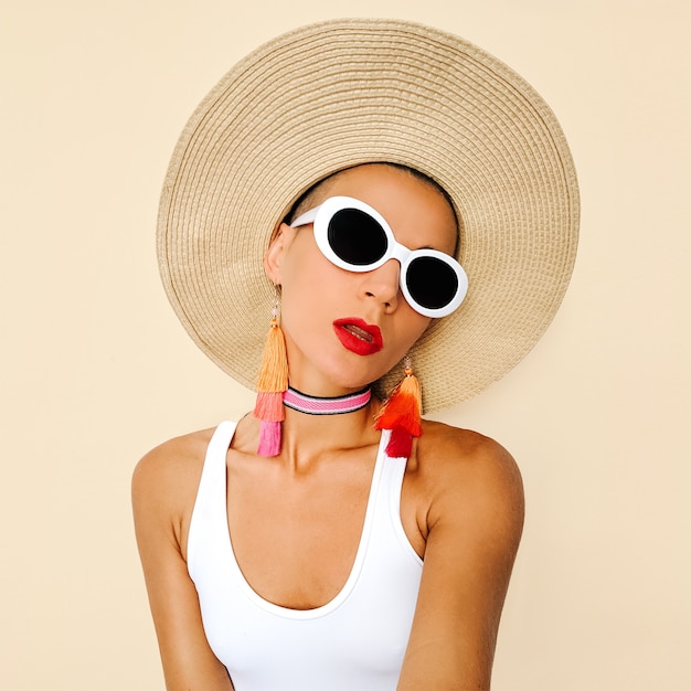 Model w stylowych akcesoriach plażowych. Okulary przeciwsłoneczne, kolczyki, kapelusz. Letni wygląd mody