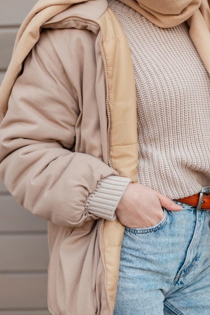 Modelka dziewczyny w modnych ubraniach z beżowym swetrem vintage, kurtką, skórzanym paskiem i klasycznymi niebieskimi dżinsami. Kobiecy styl zimowy na co dzień