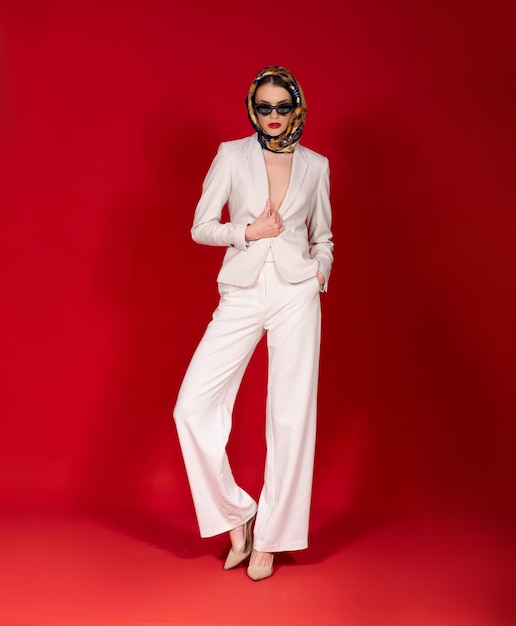 Modelka pozuje w studio w białym eleganckim stroju z szalikiem na czerwonym tle