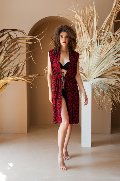 Zdjęcie modelka w czerwono-czarnej sukience stoi przed rośliną