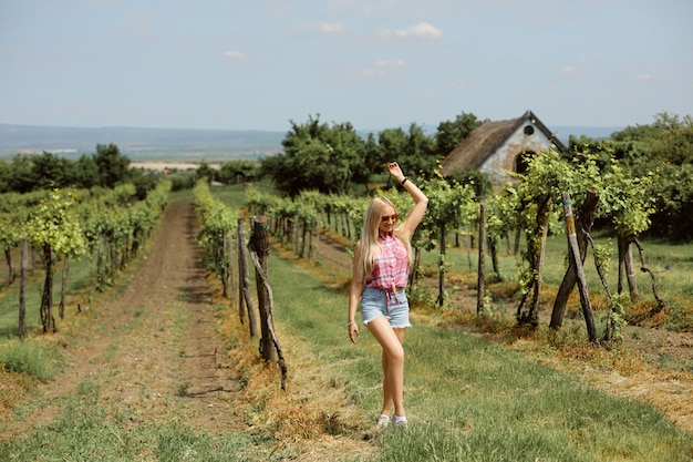 Modelka w różowej koszuli i jeansowych szortach spaceruje po wiejskiej winnicy. Koncepcja letnich podróży