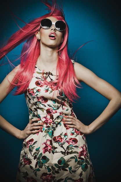 Modelka z różowymi włosami i dużymi okularami przeciwsłonecznymi na niebieskim tle