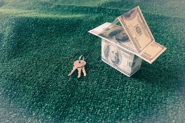 Modeluje dom i pieniądze na zielonej sztucznej trawie z kluczem