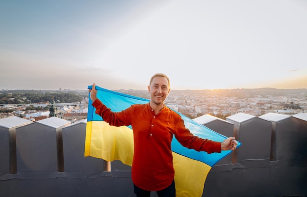 Módlcie się za UkrainexAA człowiek stoi z narodową flagą Ukrainy i macha nią modląc się o pokój o zachodzie słońca we LwowiexAA symbol niepodległości i siły narodu ukraińskiego