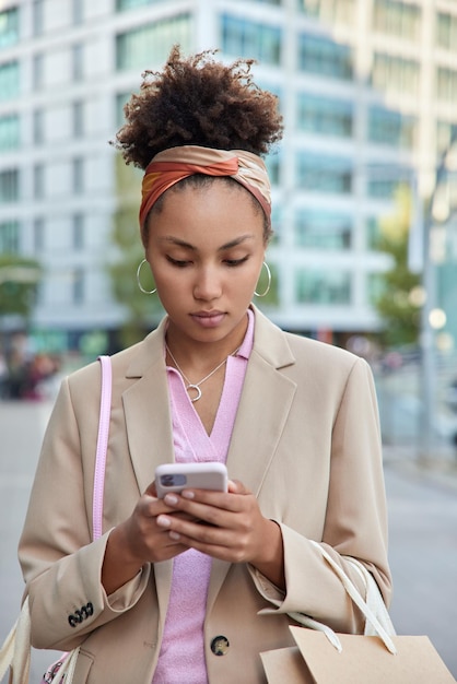 Modna Ciemnoskóra Kręcona Pani Nosi Papierowe Torby Na Zakupy Czeki Zakupy Zadowolone Z Dostawy Zarezerwowanej Przez Telefon Sprawia, że Zakupy Online Ze Zniżką Są Ubrane W Stylową Beżową Marynarkę.