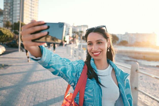 Modna, fajna i vlogująca turystka robiąca selfie telefonem na tle plaży