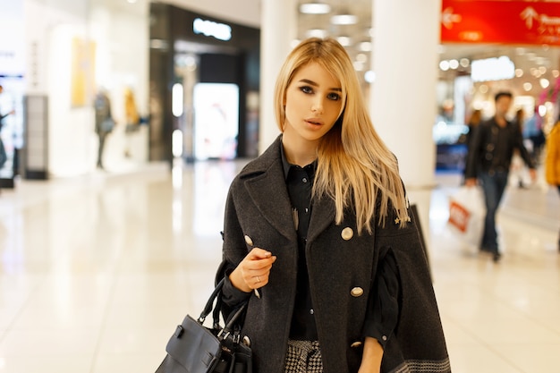 Modna kobieta w stylowym modnym płaszczu z torebką w centrum handlowym