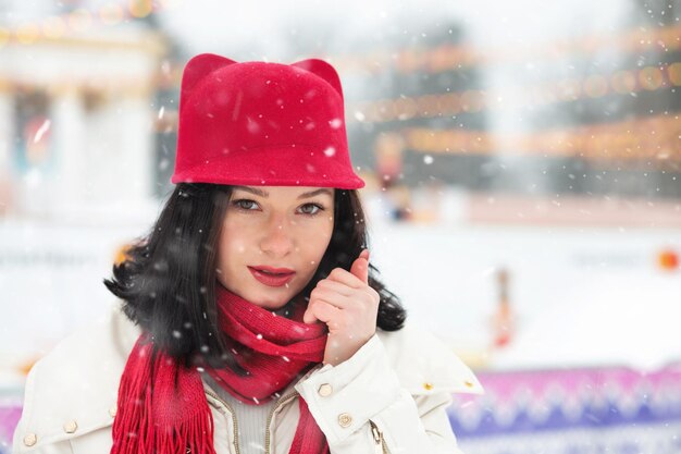 Modna młoda kobieta nosi czerwoną czapkę spacerując w winter park podczas opadów śniegu. Miejsce na tekst