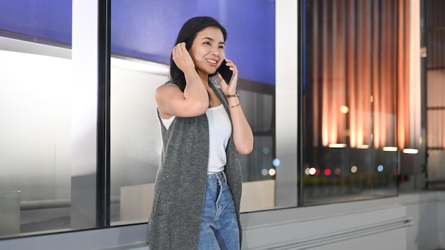 Modna młoda kobieta rozmawia przez telefon komórkowy, stojąc przed wizytówką centrum handlowego